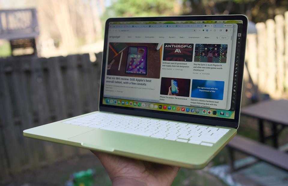 جهاز MacBook Neo الحمضي مرفوع بيد واحدة.
