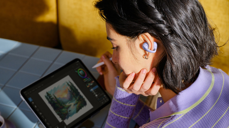 لقطة مقربة لشخص يرتدي سماعات الأذن Shokz OpenDots Air، أثناء الرسم على جهاز لوحي