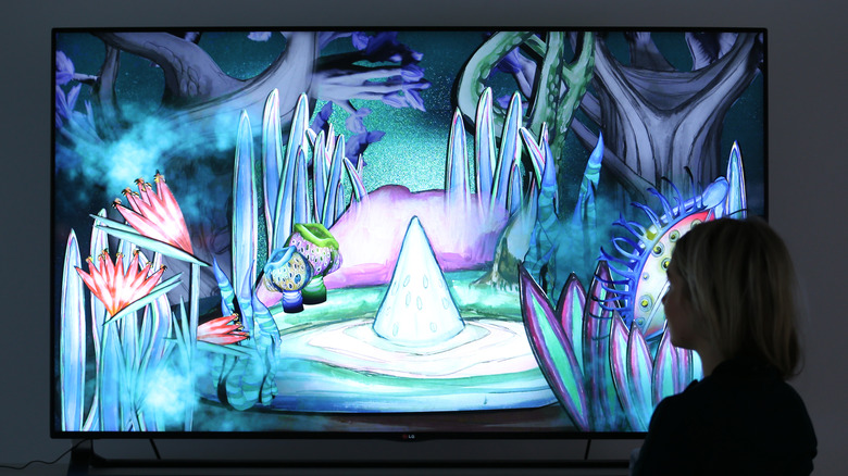 امرأة تقف أمام تلفزيون OLED وتعرض قطعة فنية ملونة وتجريدية.