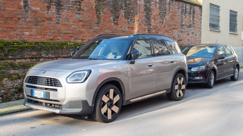 سيارة Mini Countryman SE ALL4 باللون الرمادي متوقفة في الشارع أمام جدار من الطوب